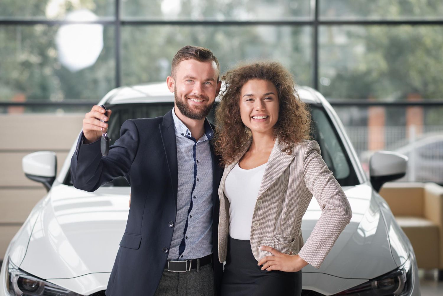 A man and a woman are standing in front of a car holding the keys.