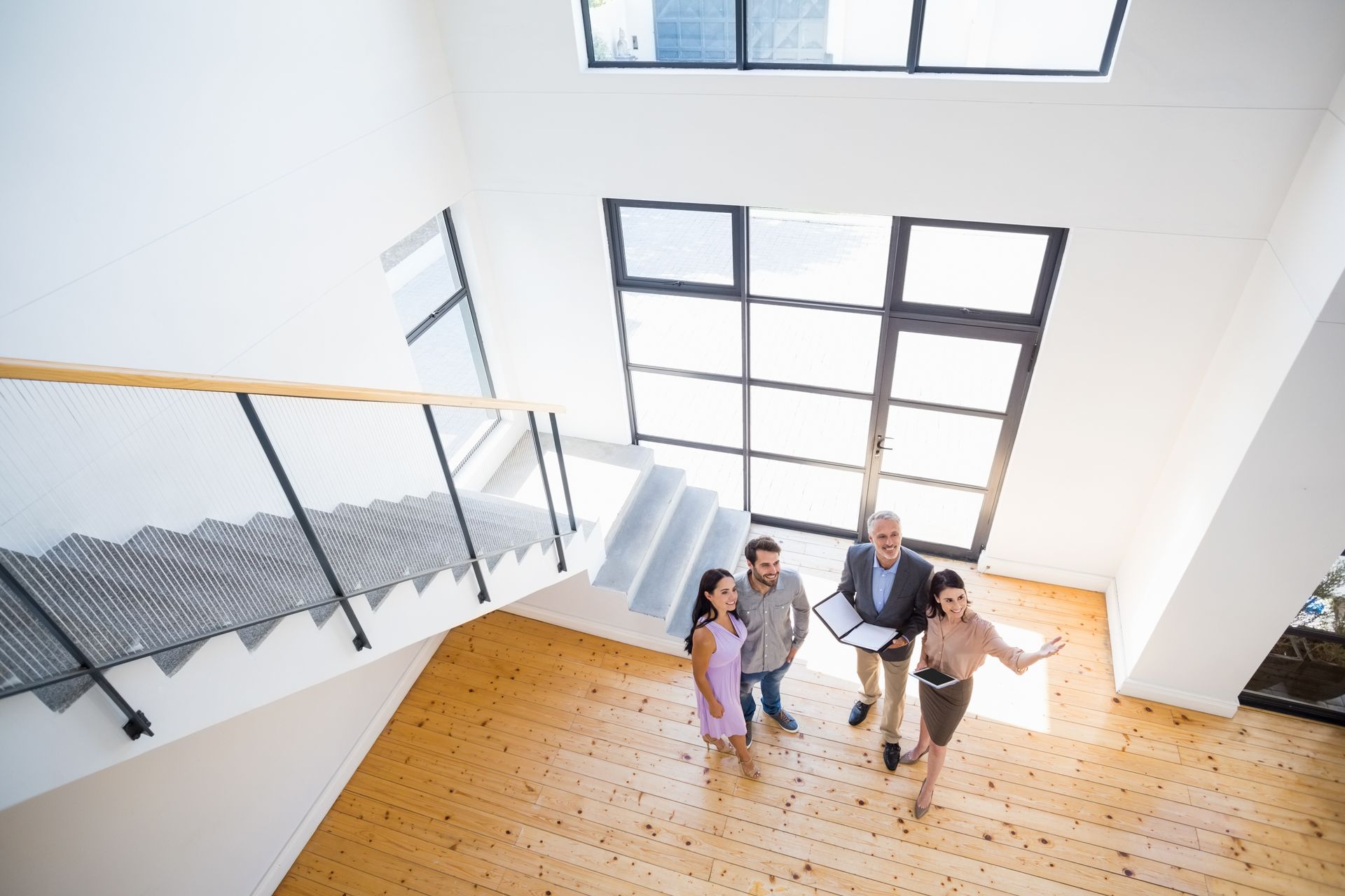 People standing on a bright staircase landing near large windows, looking up at the camera