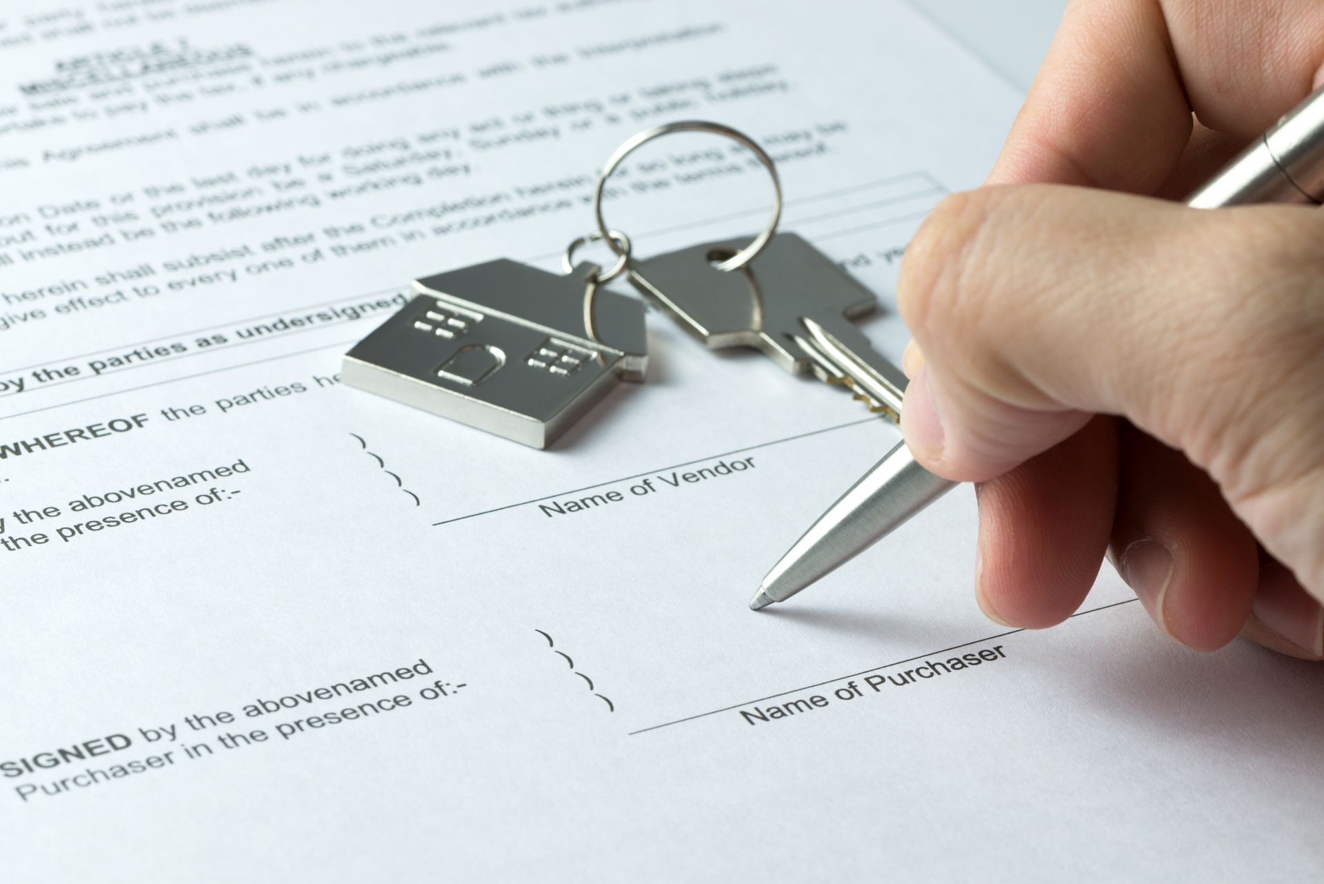 Hand signing a document beside keys and a key fob on a desk