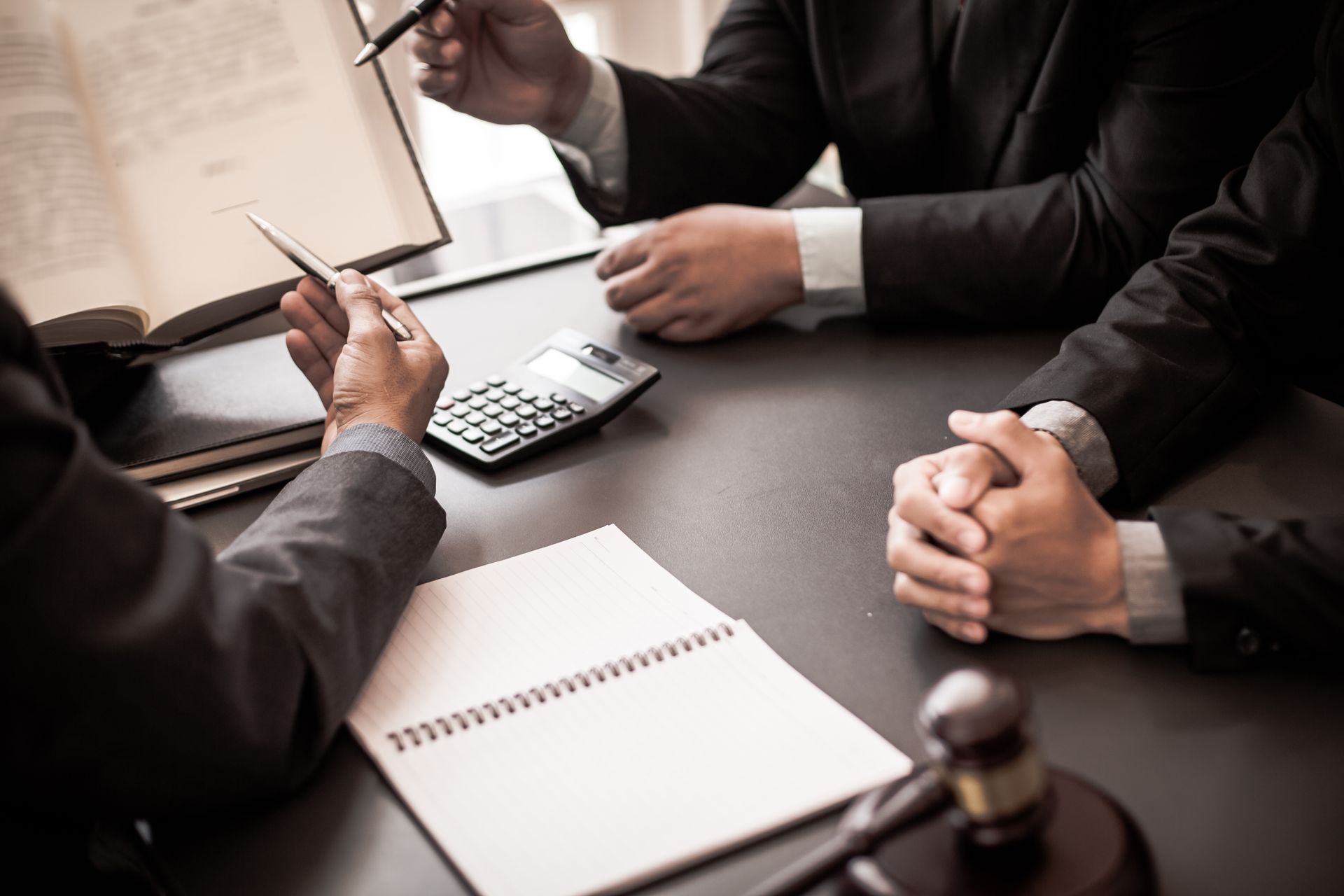 People in suits meeting at table with papers, calculator, and gavel.