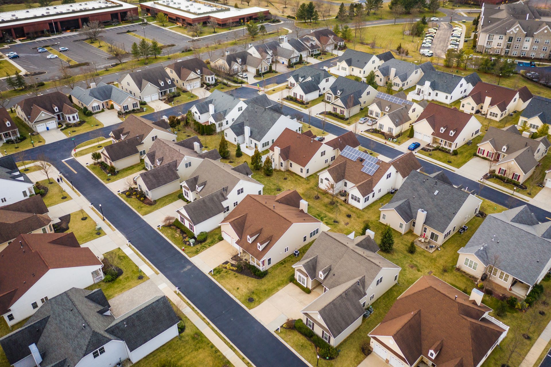 Aerial view of a suburban neighborhood with rows of houses, roads, and a commercial building.