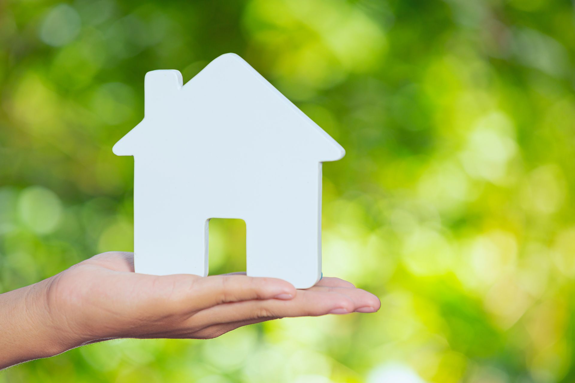 Hand holding a white house cutout against a green blurred background