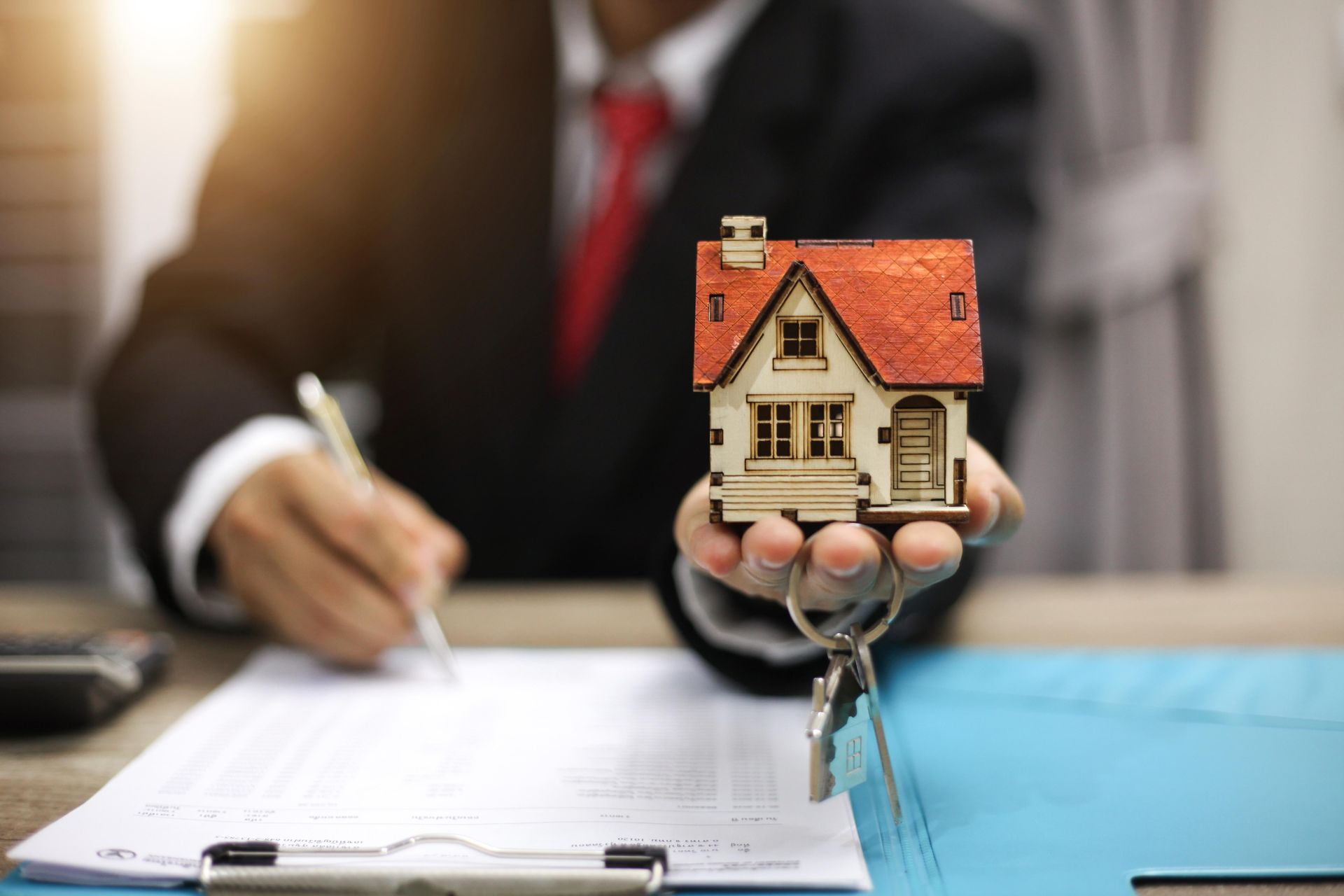 Real estate agent holding house model and keys, signing documents.