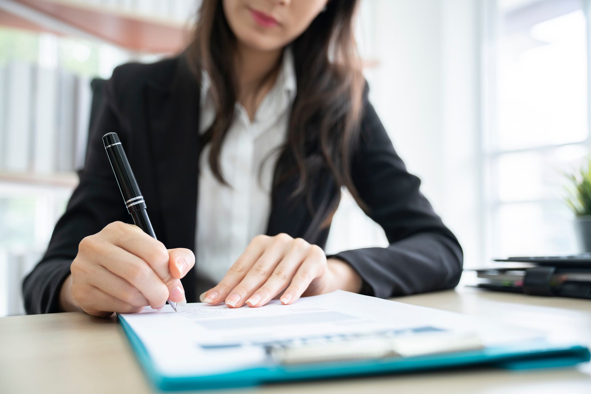 A woman is sitting at a desk signing a document with a pen.