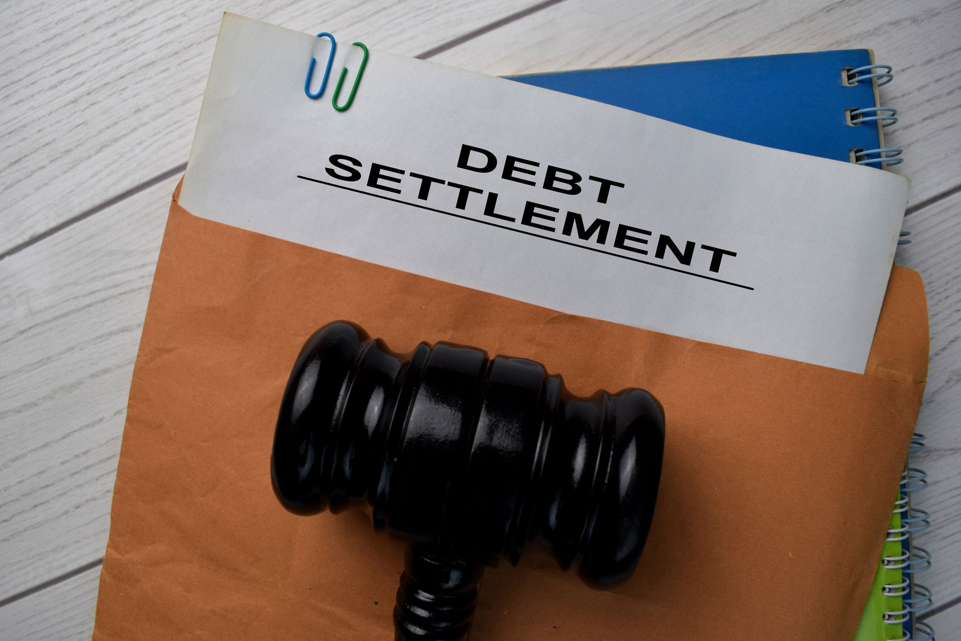 Debt settlement document in an envelope with a gavel on a light wood surface.