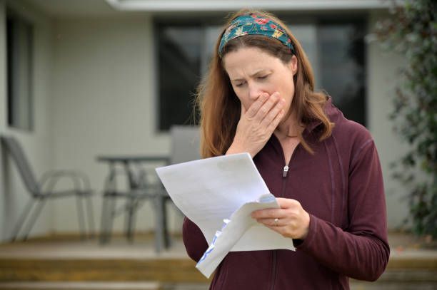 A woman is covering her mouth while reading a piece of paper.