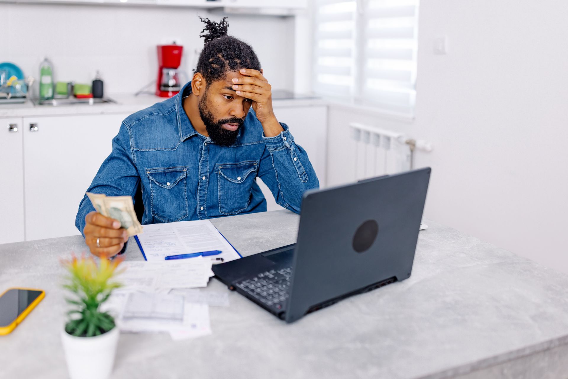 A man is sitting at a table with a laptop and holding money.