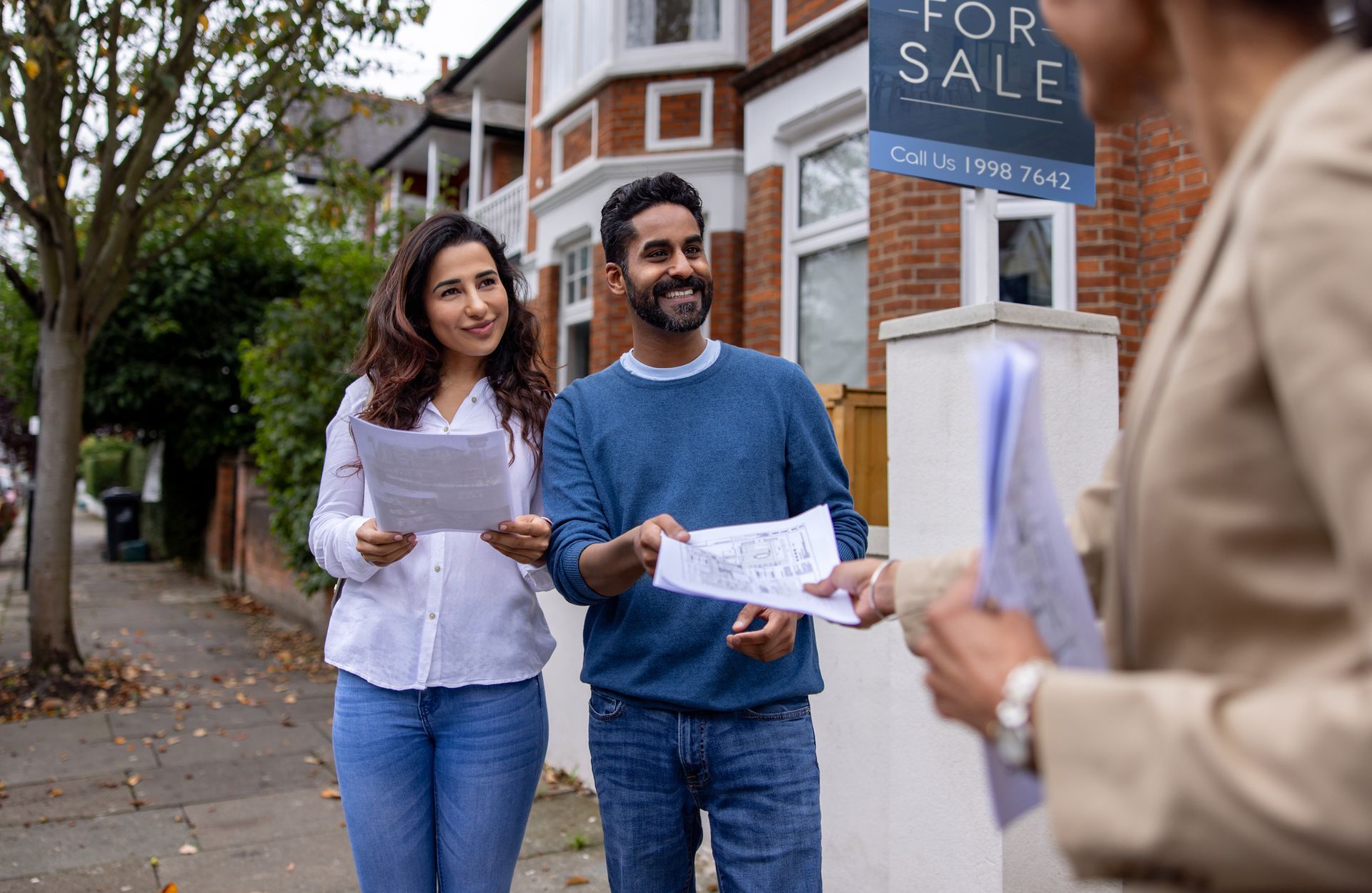 A man and a woman are standing in front of a house for sale.