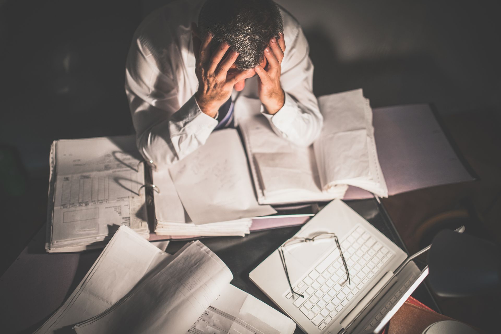 A man is sitting at a desk with his head in his hands.
