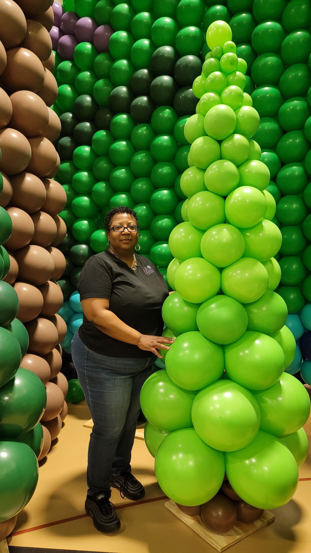 a woman is standing next to a large green balloon tree .