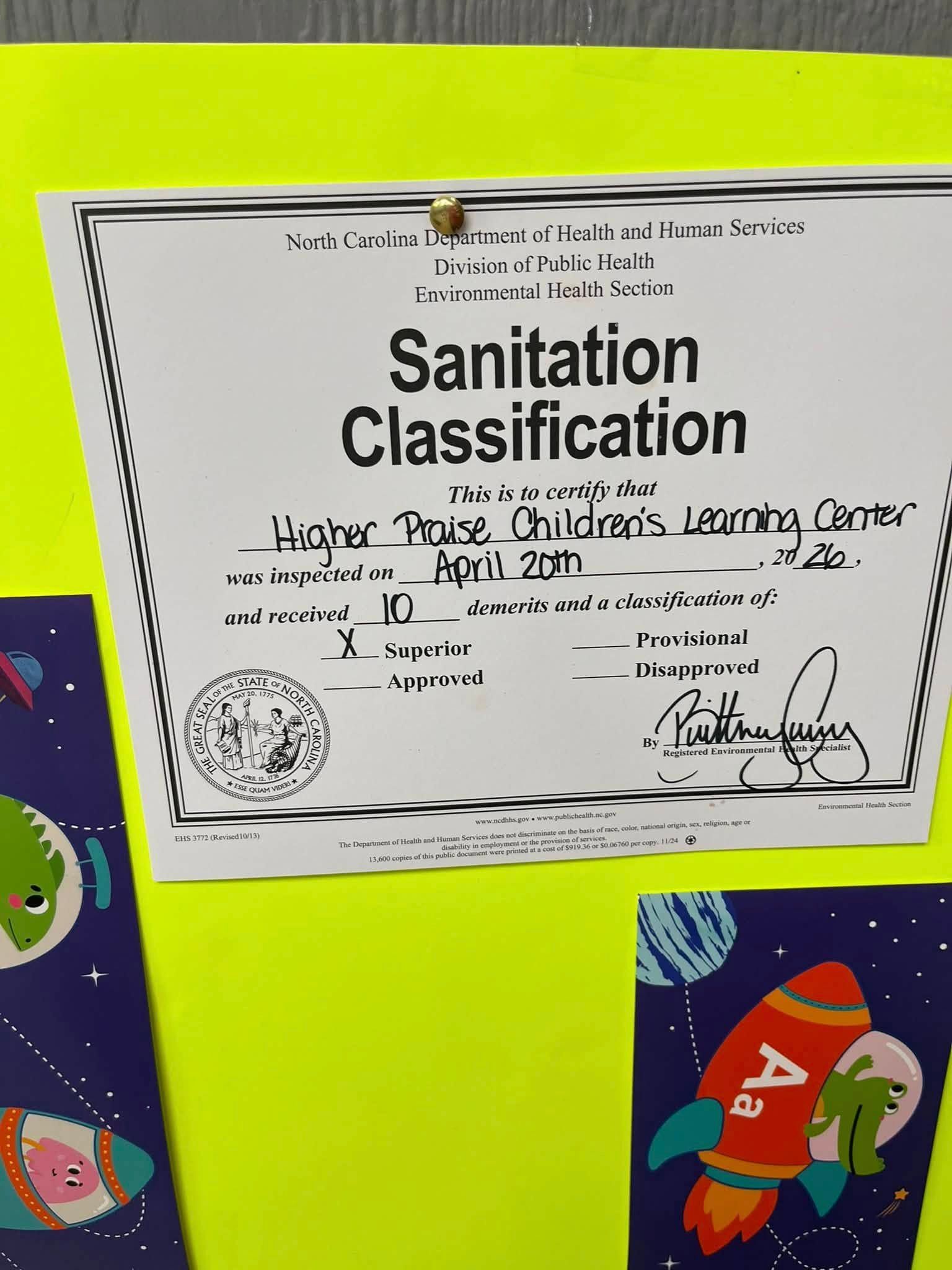 Certificate titled “Sanitation Classification” pinned on a bright yellow board with colorful children’s drawings.