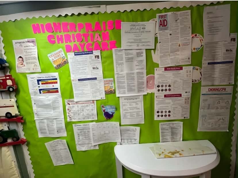 Green bulletin board with posters and papers, titled “Higher Brain Christian Daycare,” above a small white table.
