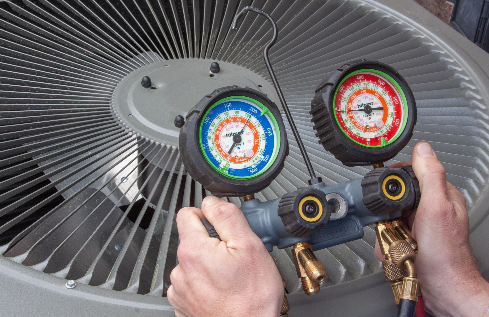 A person is holding two gauges in front of an air conditioner. HVAC Maintenance Wilmington NC