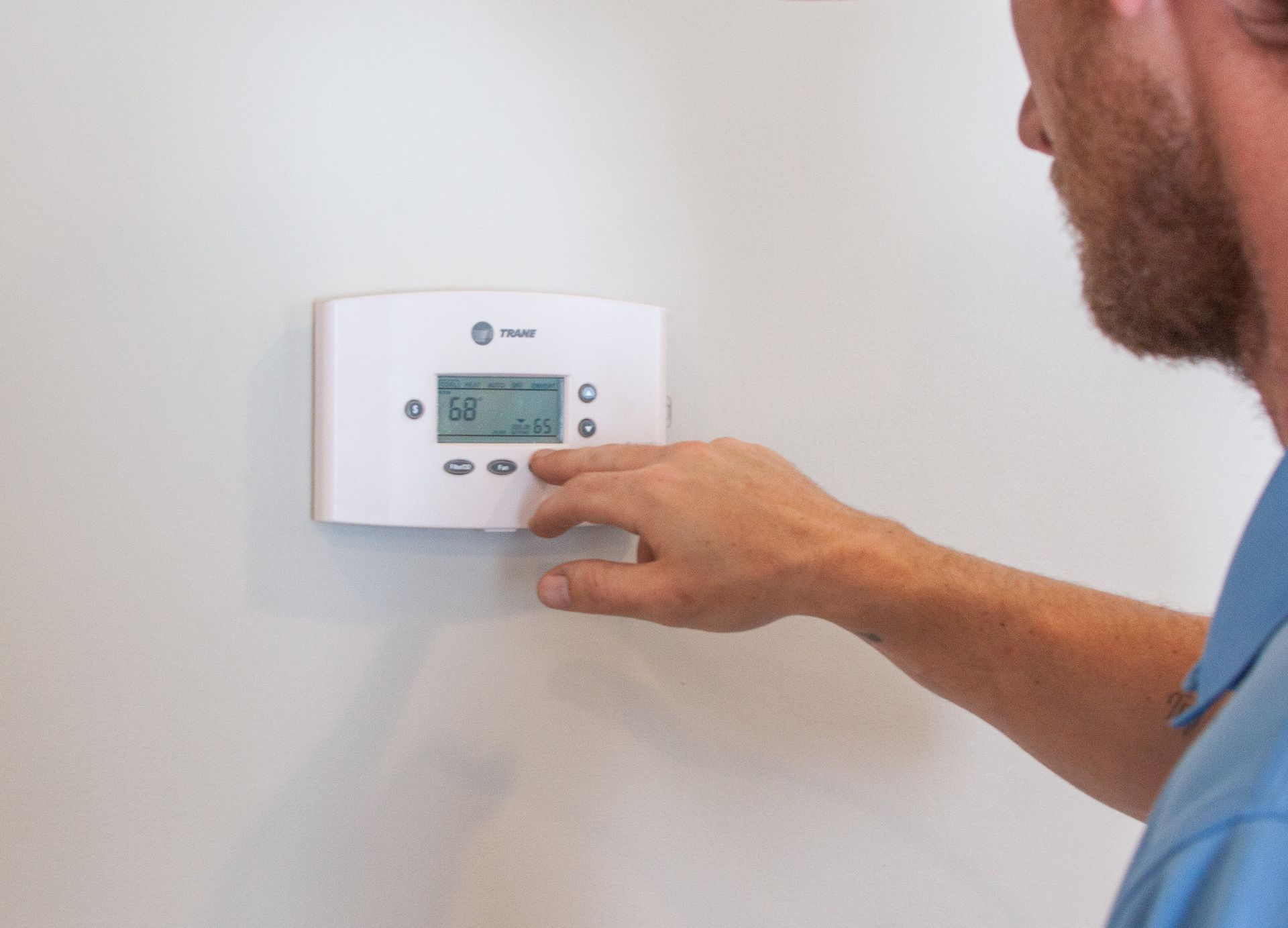 A man is adjusting a thermostat on a wall. Programming a Replacement Thermostat after Installation Wilmington NC