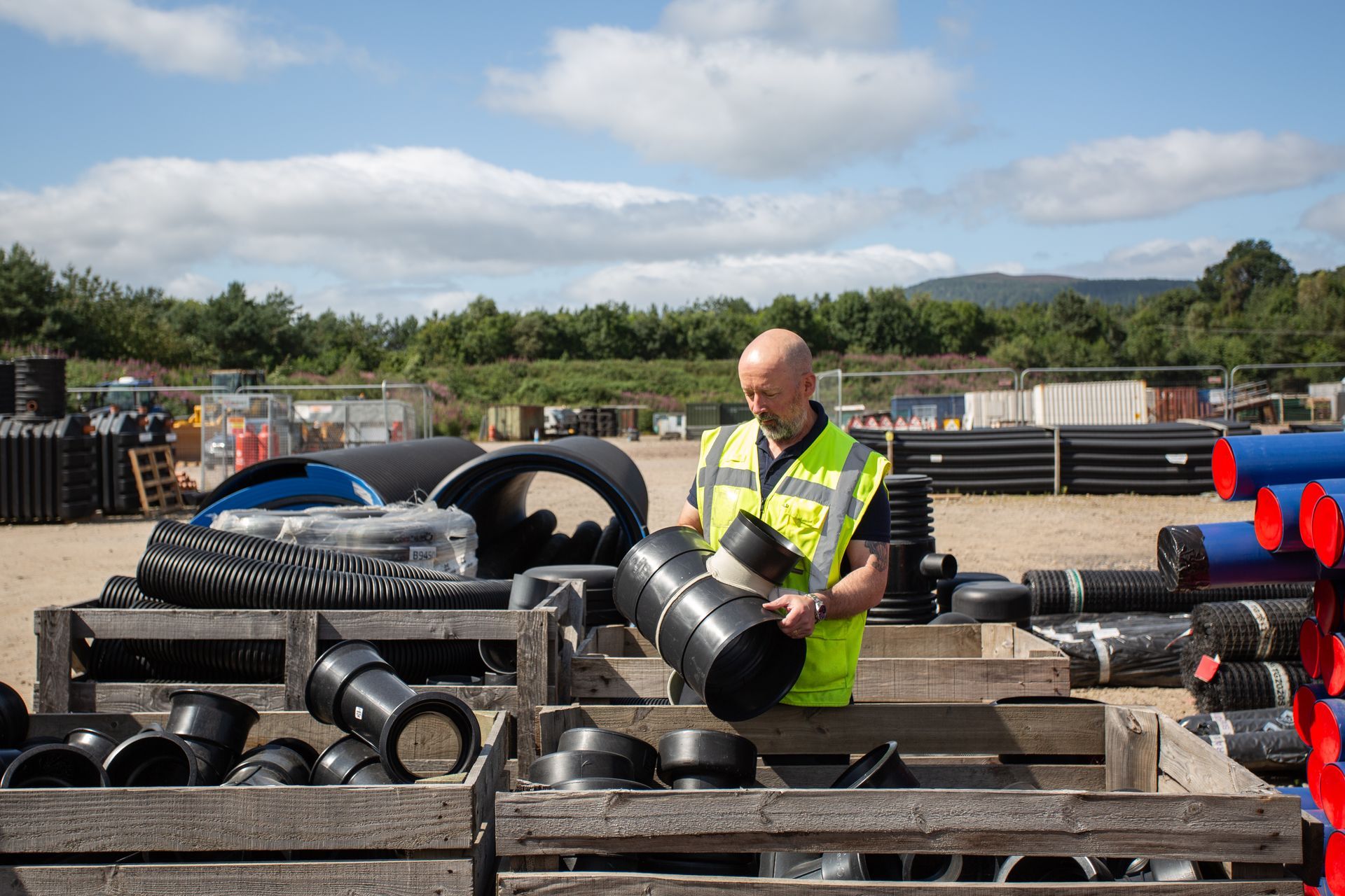 A man in a yellow vest is standing in front of a pile of pipes.