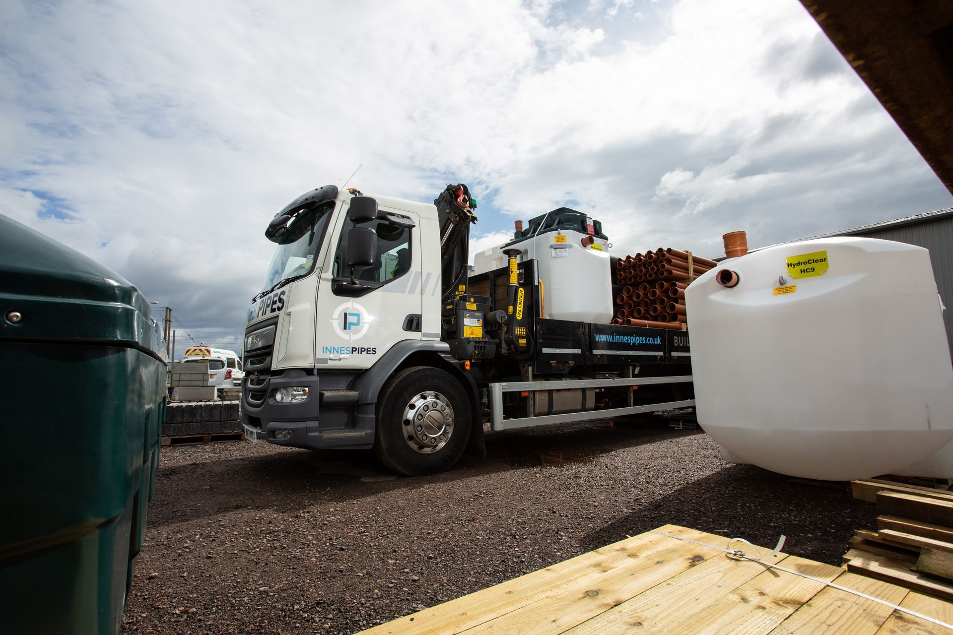 A white truck is parked in a gravel lot next to a large white tank.