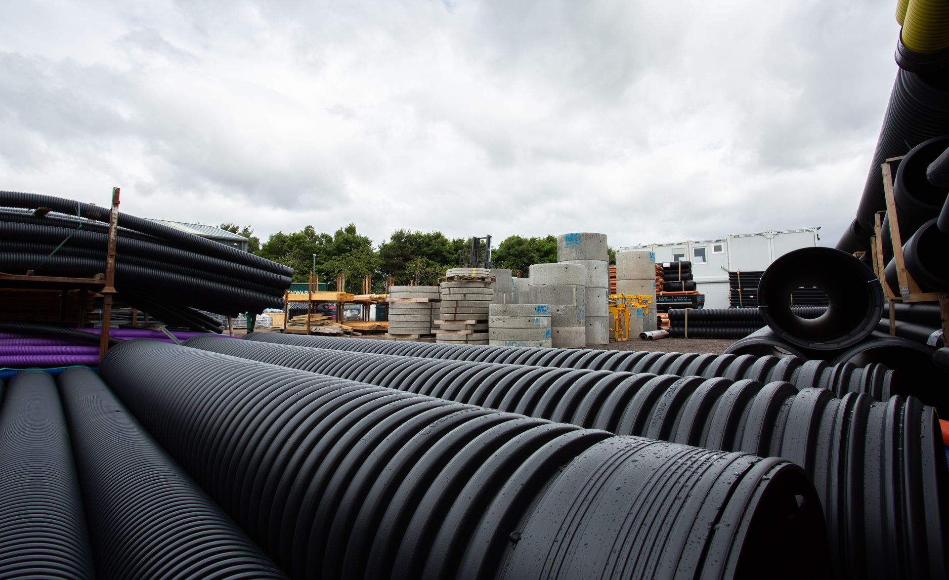 A bunch of black pipes are stacked on top of each other in a yard.