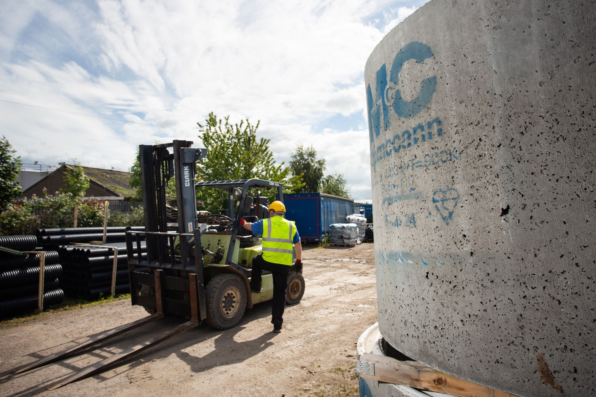 A man in a yellow vest is standing next to a forklift.