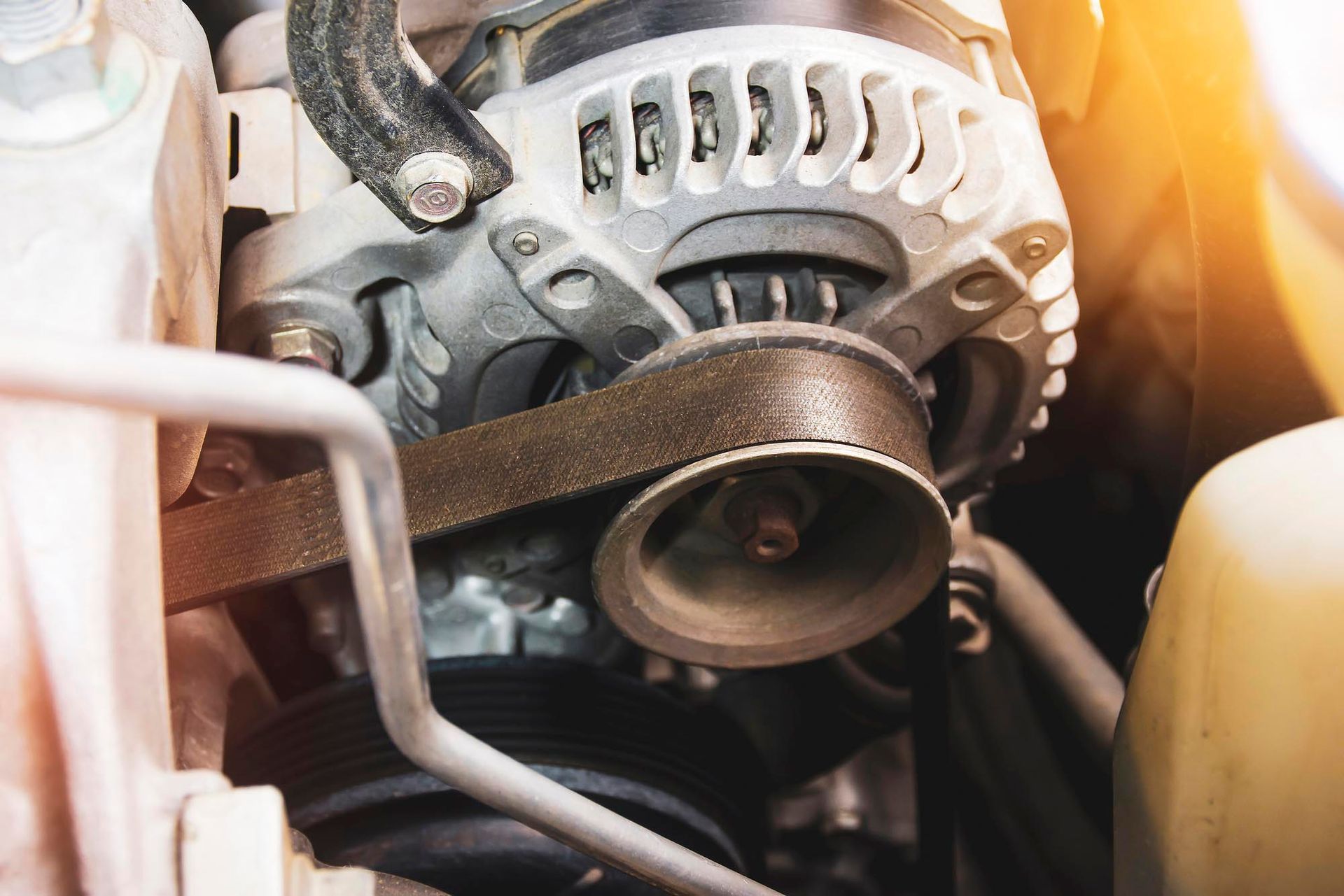 A close up of an alternator and belt on a car engine.