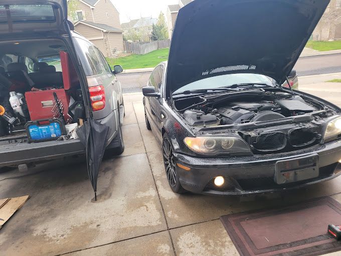 A black car with the hood up is parked in a driveway.