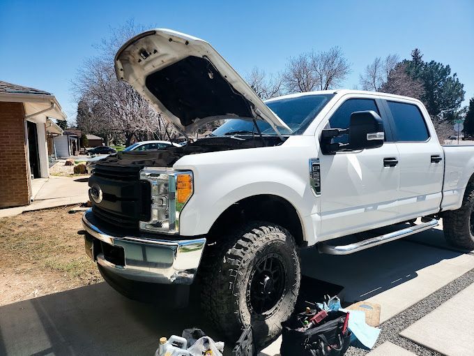 A white truck with the hood up is parked in a driveway.