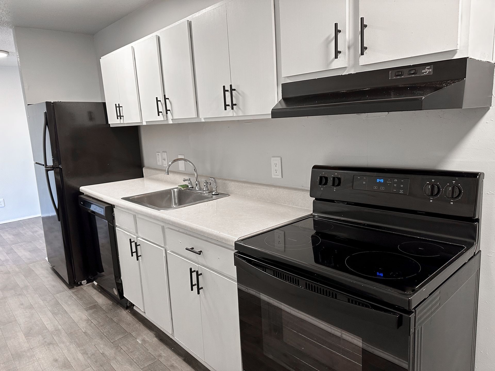 A kitchen with white cabinets , a black stove , a black refrigerator and a black dishwasher.