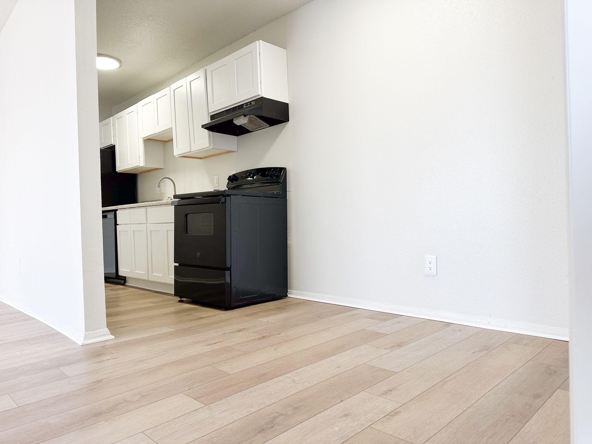 An empty kitchen with a black stove and white cabinets.