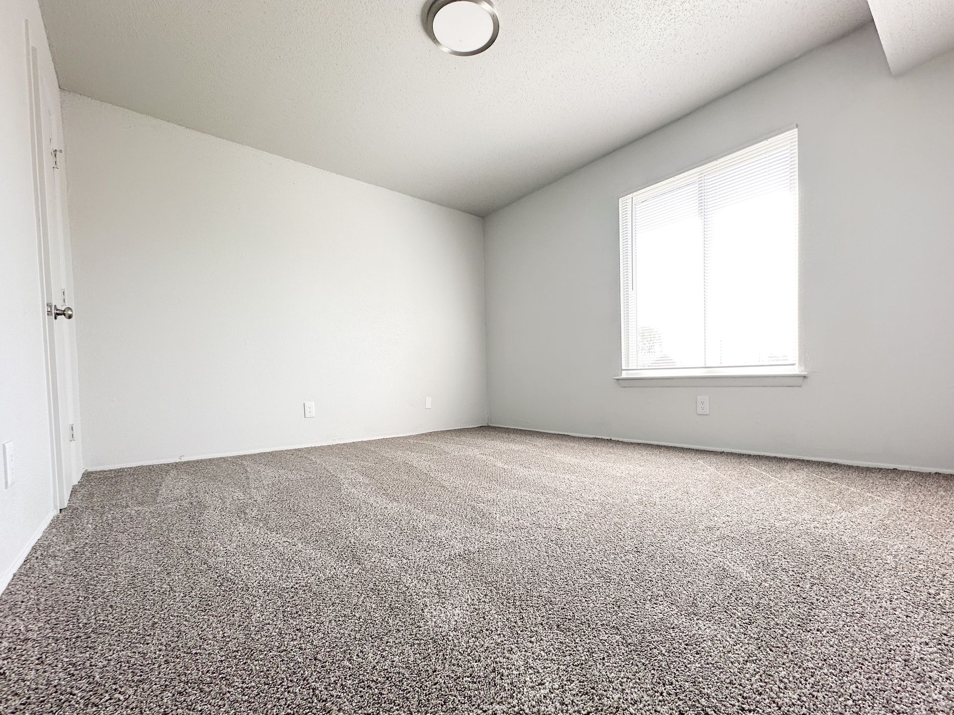 An empty bedroom with a carpeted floor and a window.