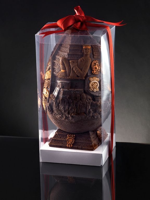 Uovo di cioccolato a tema Maya, in scatola trasparente con nastro rosso.