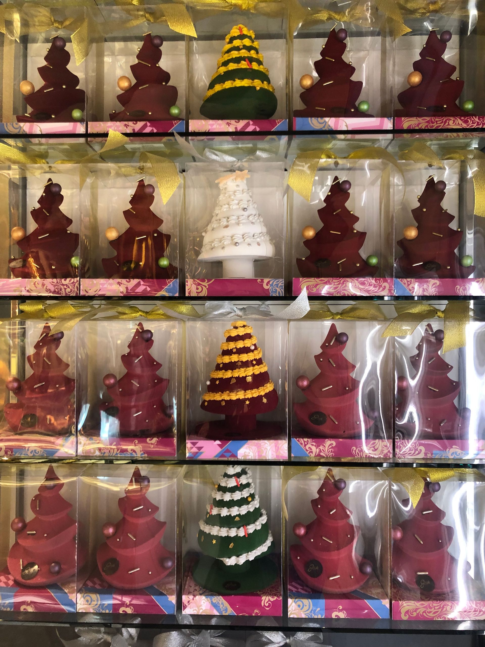 Cioccolatini a forma di albero di Natale in scatole trasparenti, disposti in file. Alcuni sono rossi, verdi e gialli.