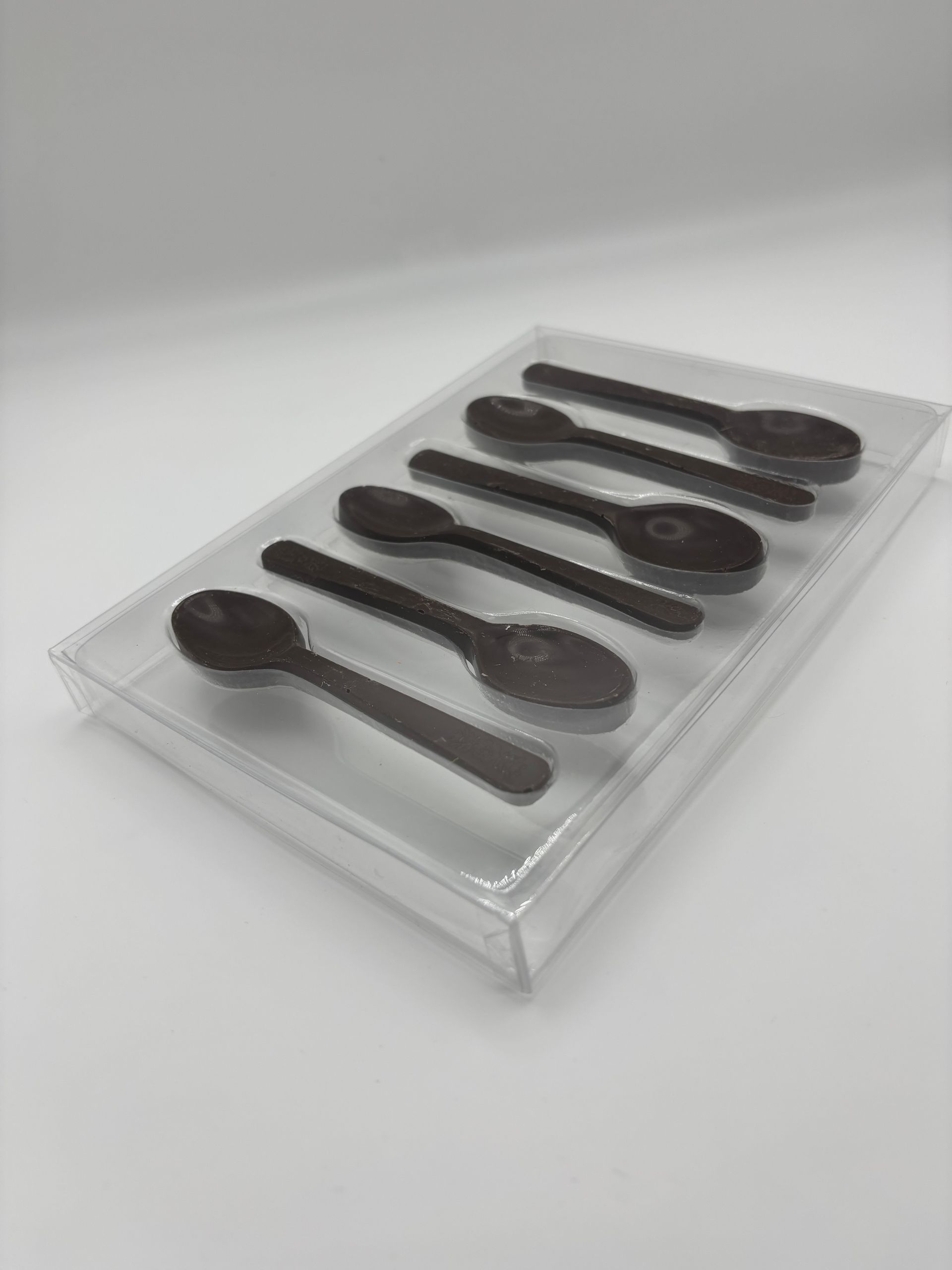 Sei cucchiaini di cioccolato in una scatola di plastica trasparente, disposti su uno sfondo bianco.