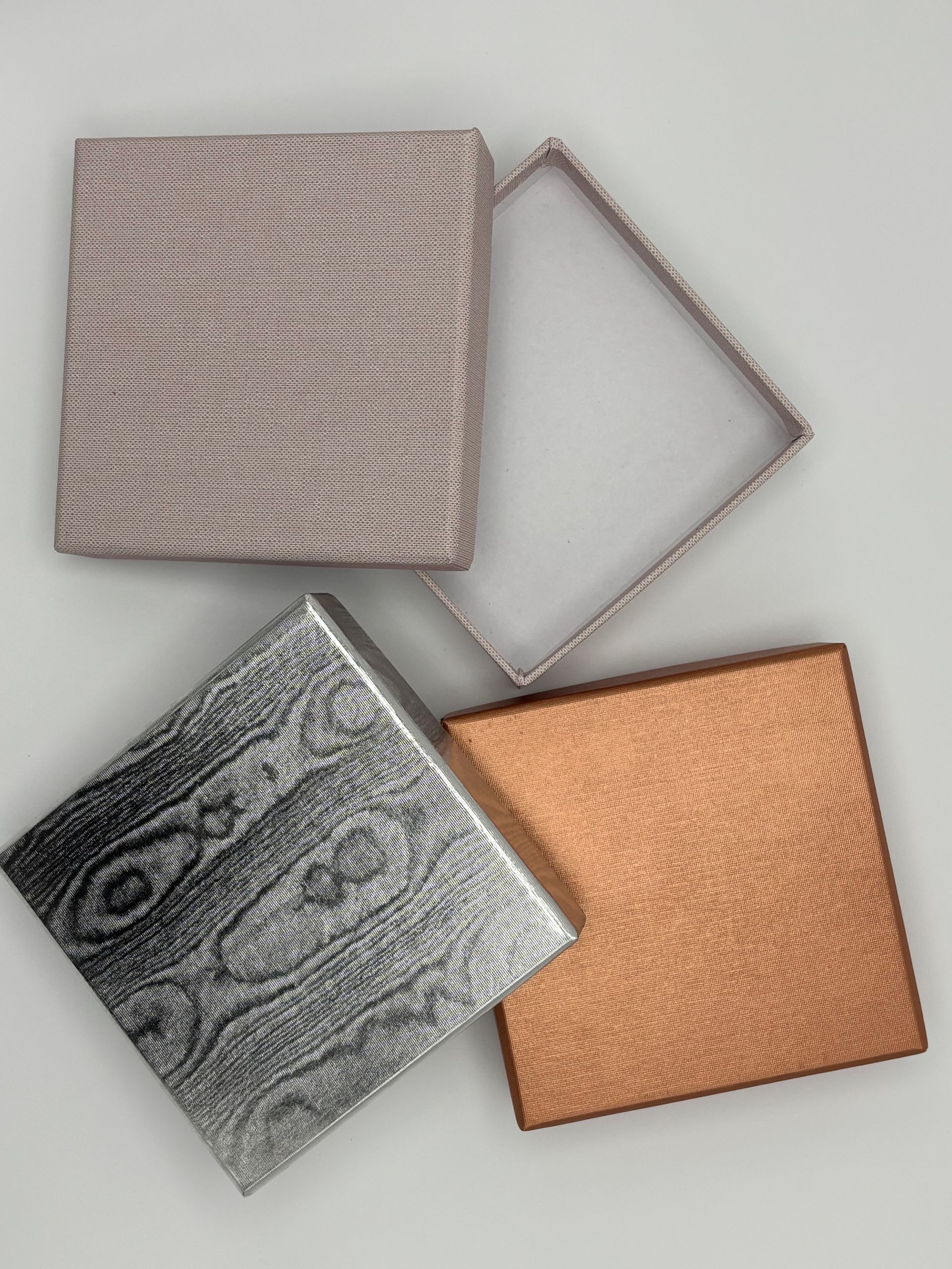 Quattro scatole quadrate decorate in argento, rame e marrone chiaro. Una scatola è aperta.