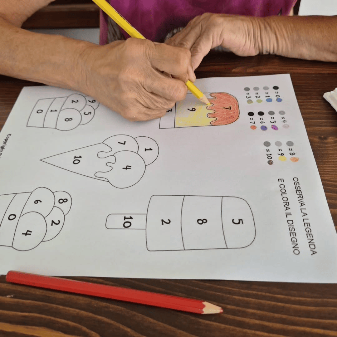 Persona che colora un foglio di gelato da colorare con una matita gialla; su un tavolo di legno.