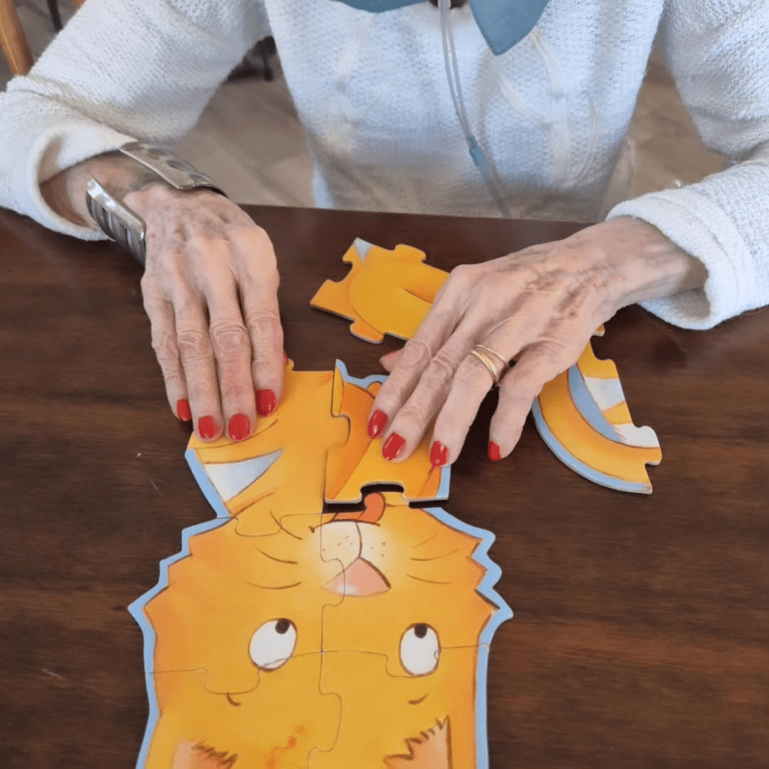 Una donna con le unghie rosse sta componendo un puzzle a forma di gatto su un tavolo marrone.