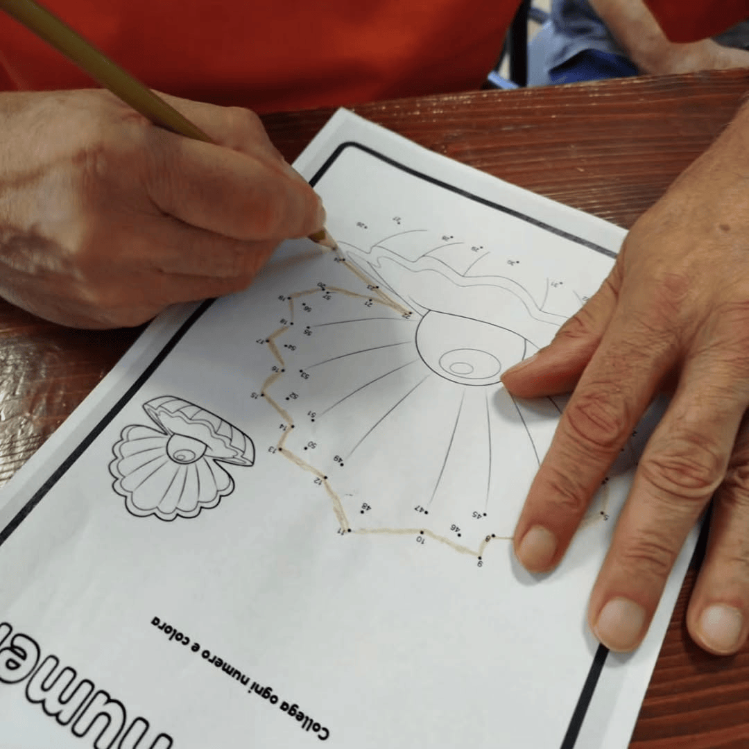Mani di una persona che collegano i punti per formare una conchiglia, usando una matita. Foglio di lavoro su un tavolo.