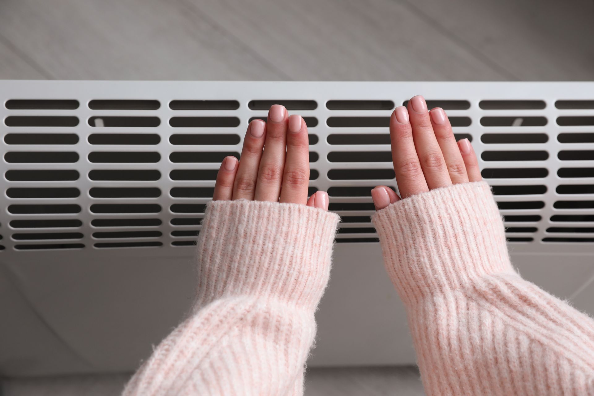 Woman warming hands near Airmax electric heater at home.