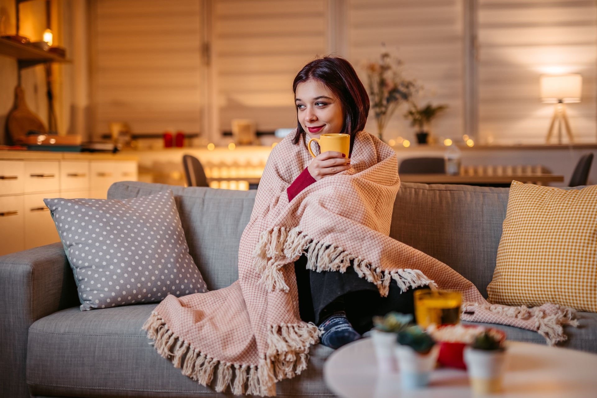 Woman drinking hot tea wrapped in blanket after technician performed a heating tune-up on a resident