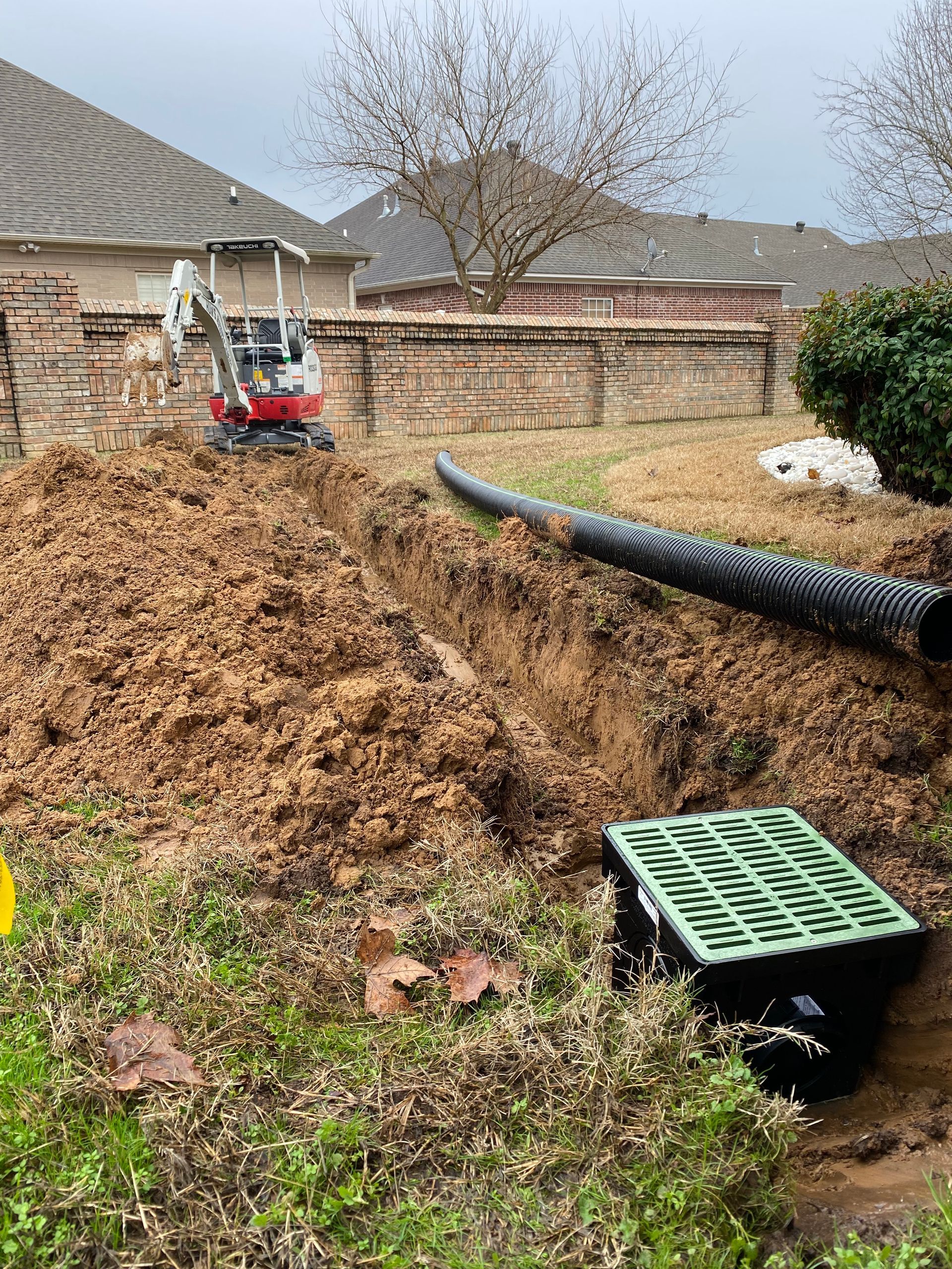 A small excavator is digging a hole in the dirt in front of a house.