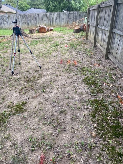 a tripod is sitting in the middle of a yard next to a wooden fence ready to have drainage solution consultation.