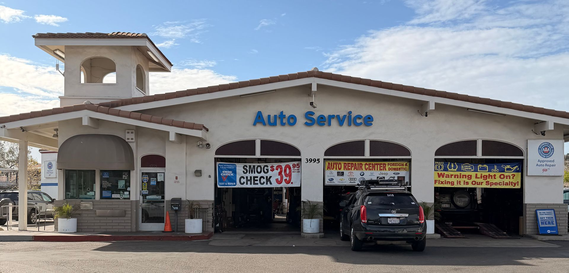 A tan, single-story auto service center with a prominent tower feature and three service bays under a blue sky.