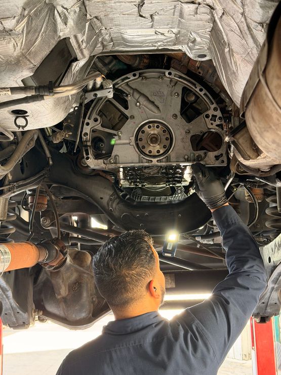 A mechanic works on the undercarriage of a vehicle, inspecting the exposed rear of an engine block.