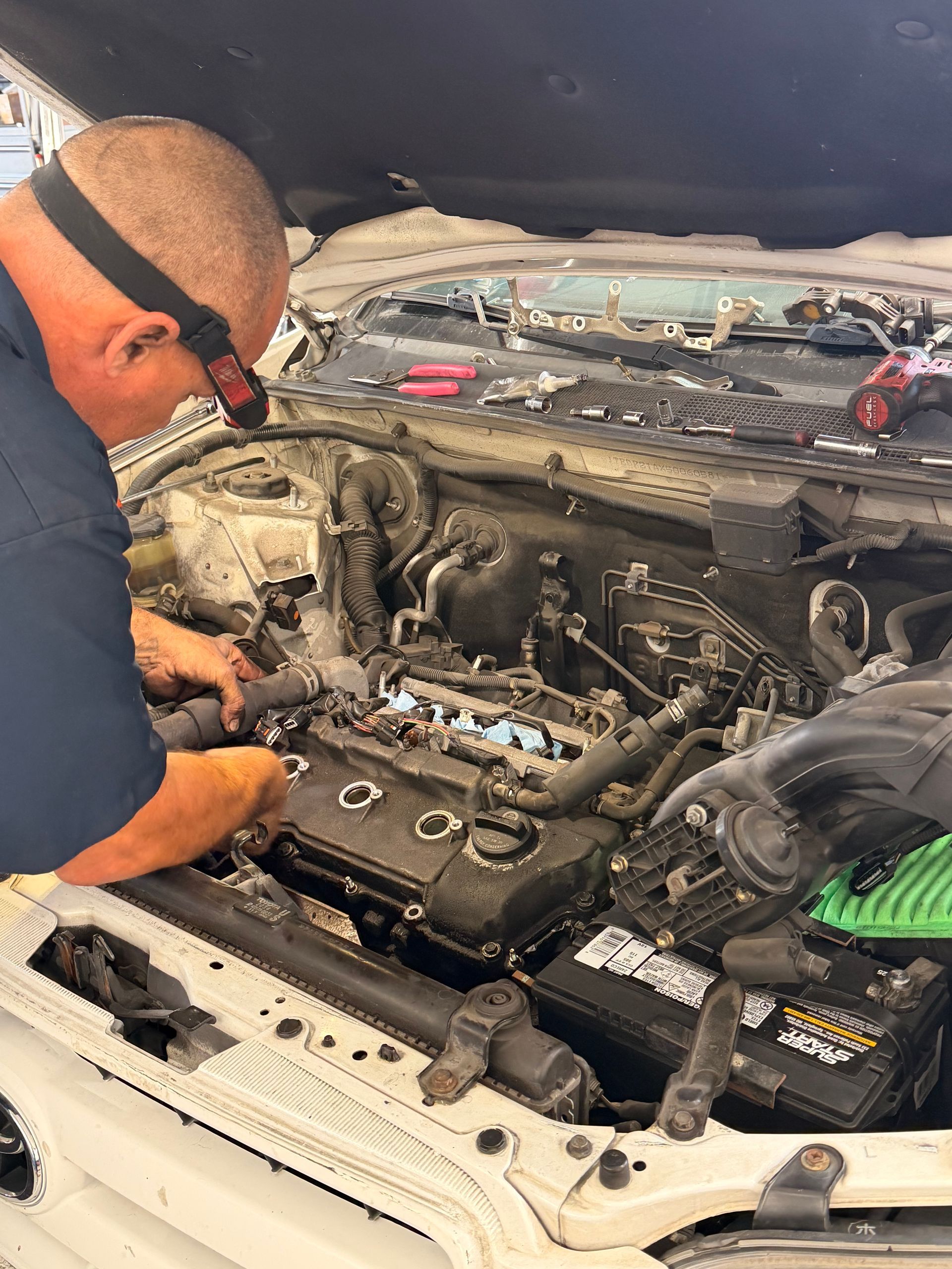 A mechanic in a blue shirt works on the engine of an open-hood vehicle in a shop.