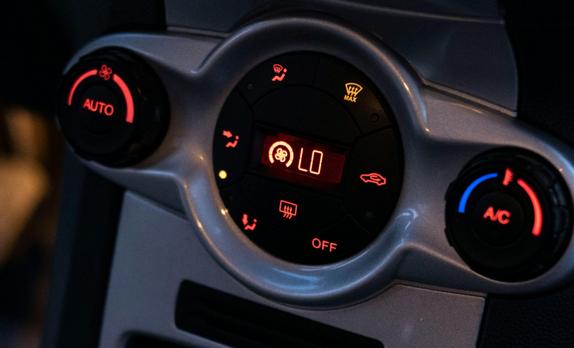 A car's silver climate control console with glowing orange buttons and a digital display set to 