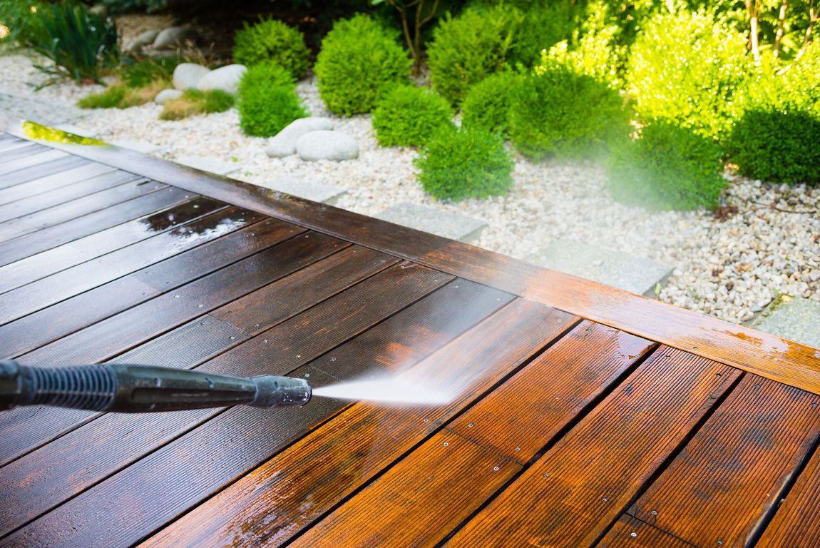 A person is using a high pressure washer to clean a wooden deck.