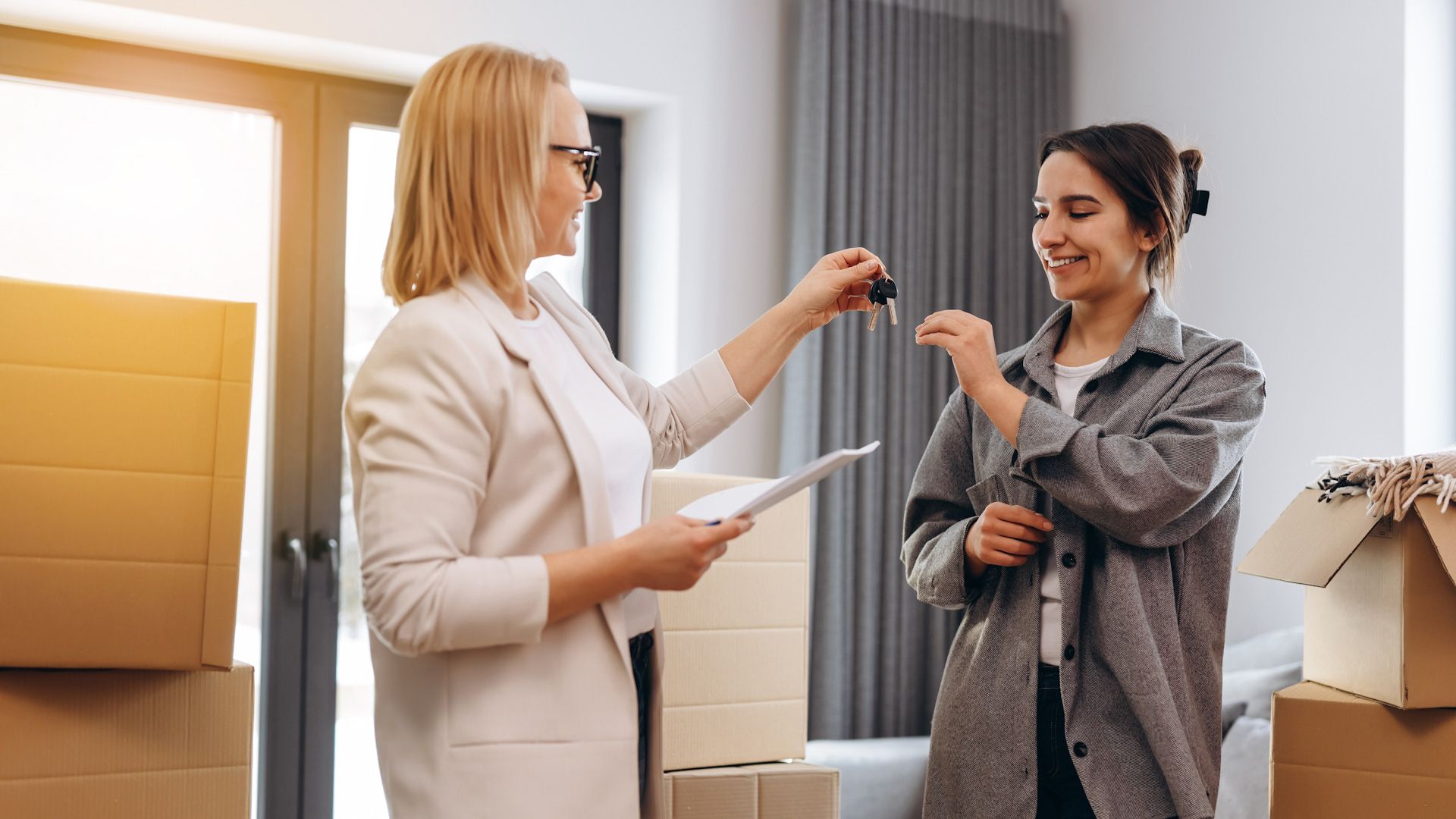 A woman is giving a key to another woman in a living room.