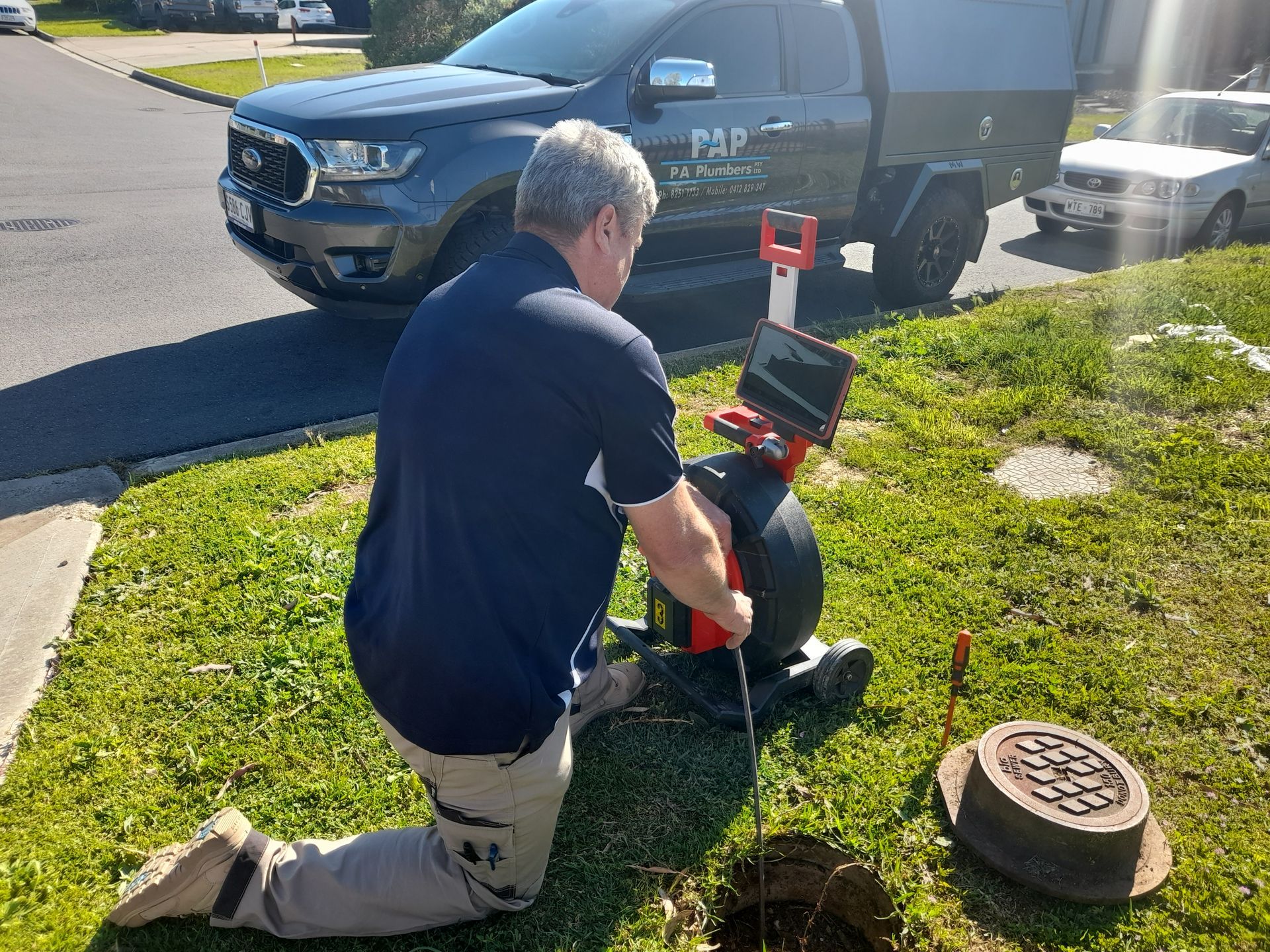 A man is kneeling down in front of a truck while using a camera.