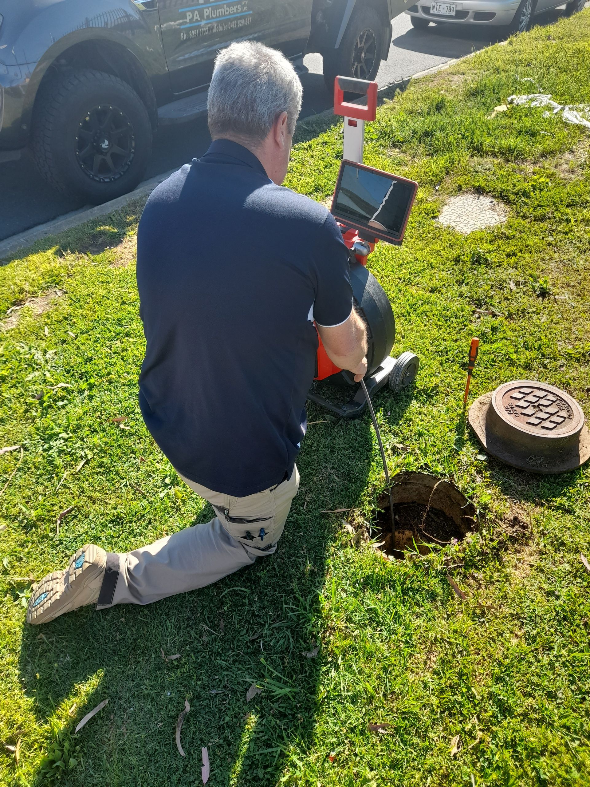 A man is kneeling down in the grass looking at a laptop.