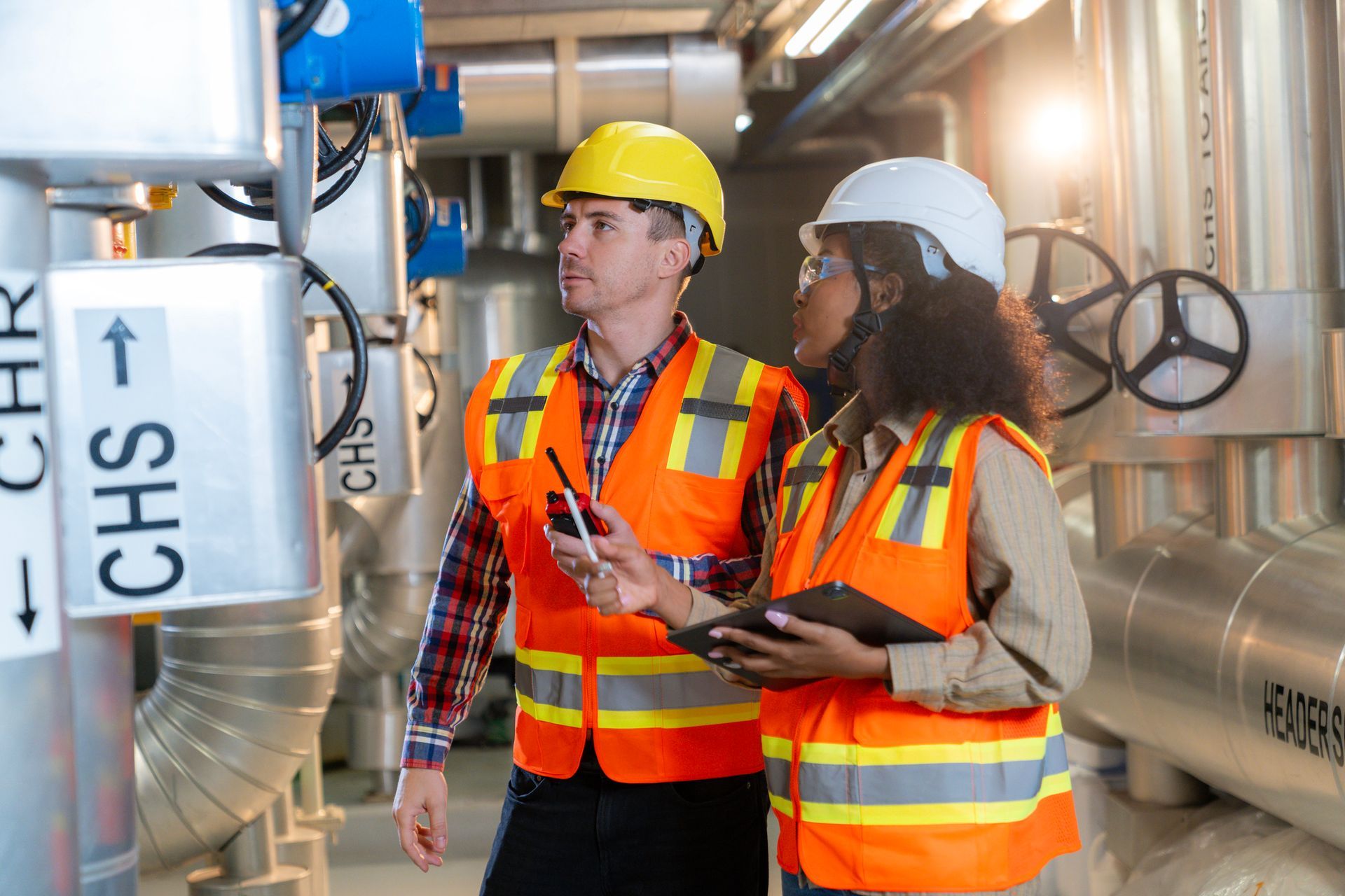 Engineers inspecting pipes during hot water system installation in industrial facility.
