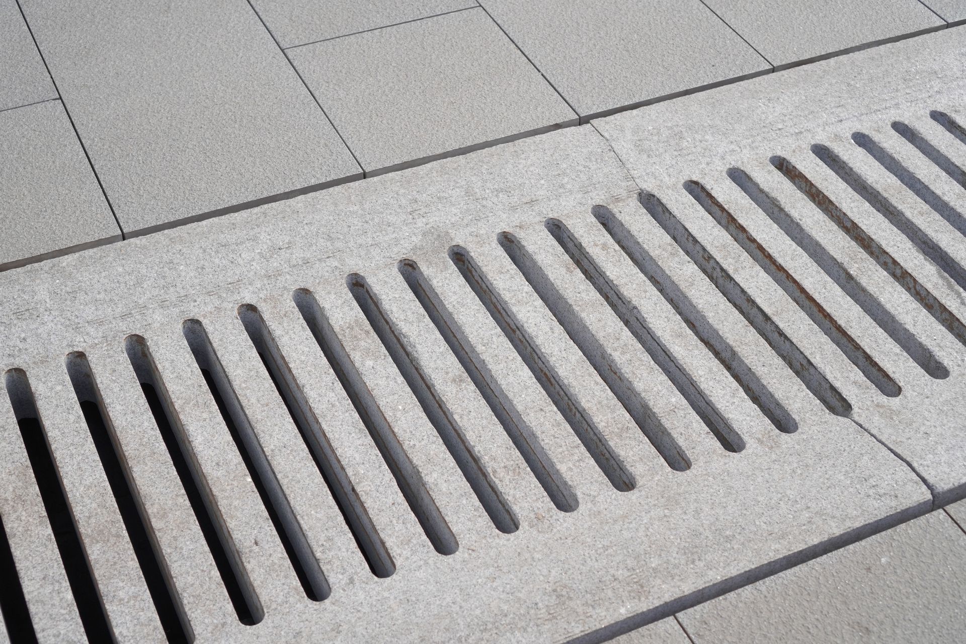 Metal drainage grate on a tiled sidewalk.