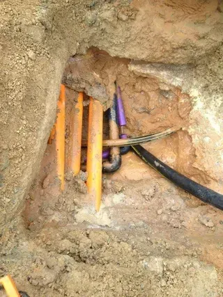Orange conduits, purple and black pipes in an excavated trench, in the ground.